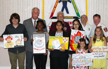New Jersey Department of Community Affairs (DCA) Commissioner Charles A. Richman and Acting Director and State Fire Marshal William Kramer, Jr. are standing with children who won the Scholastic Fire Prevention Poster Contest for the 2014-2015 school year.