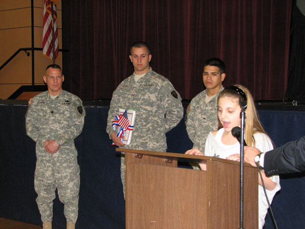 A 6th grader from Woodcliff Lake Middle School reads her letter to soldiers while Lt. Col. Mark Piterski and servicemen look on.