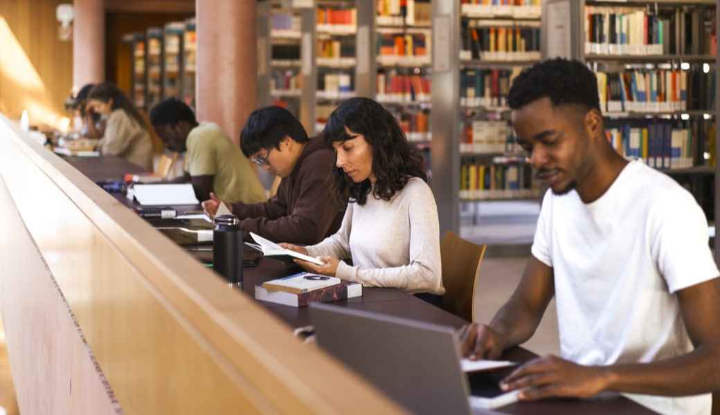 Students sitting in the library and studying on the laptop, with books and notebooks