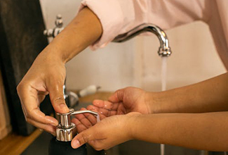 close up of a sink fauce with running water. An adult is dispensing soap into a child's hand