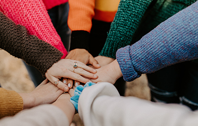 A group of students forming a circle with one of their hands in the middle.