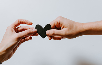 Two hands holding a paper heart between them.