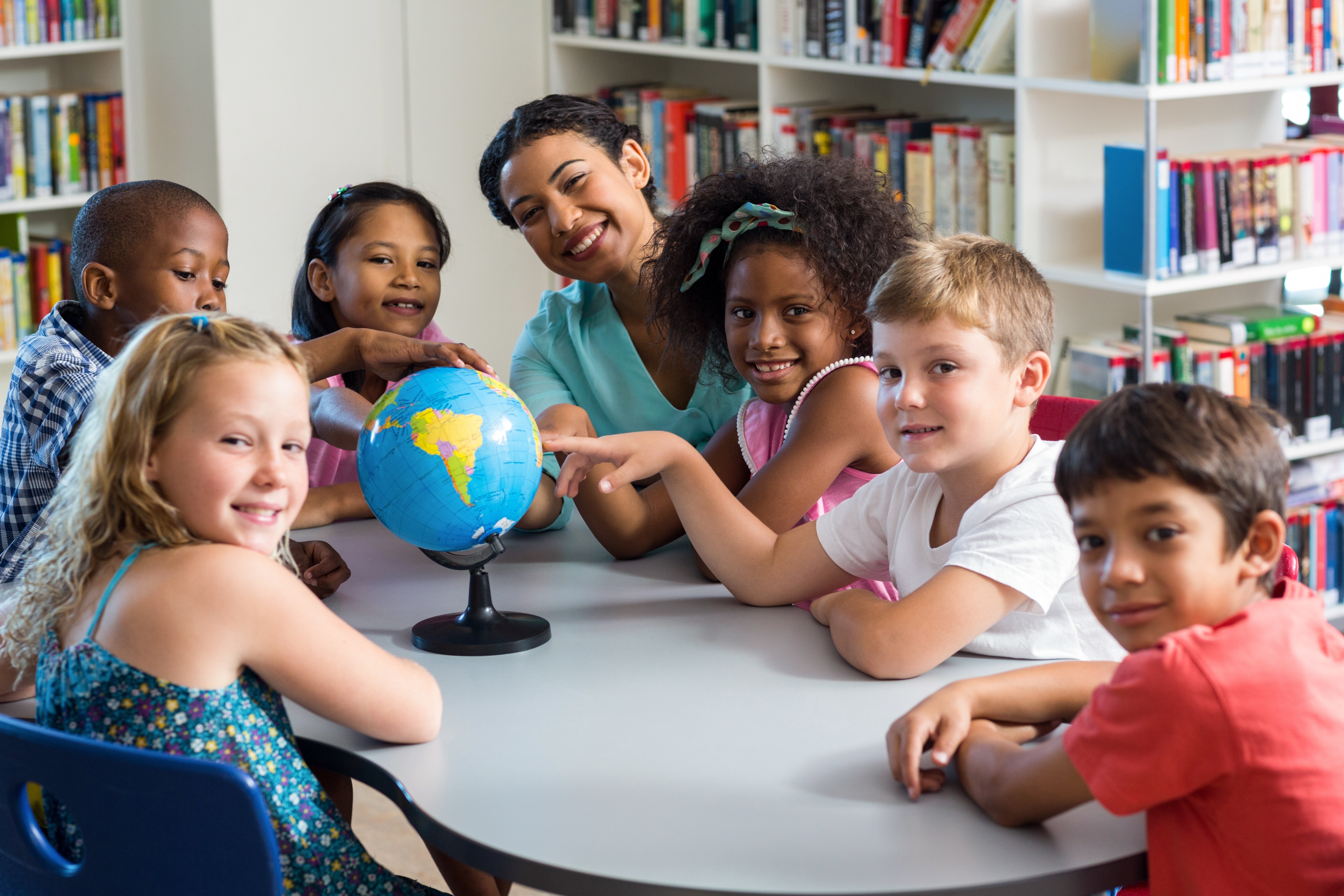 Elementary students at a table with a teacher looking at a globe
