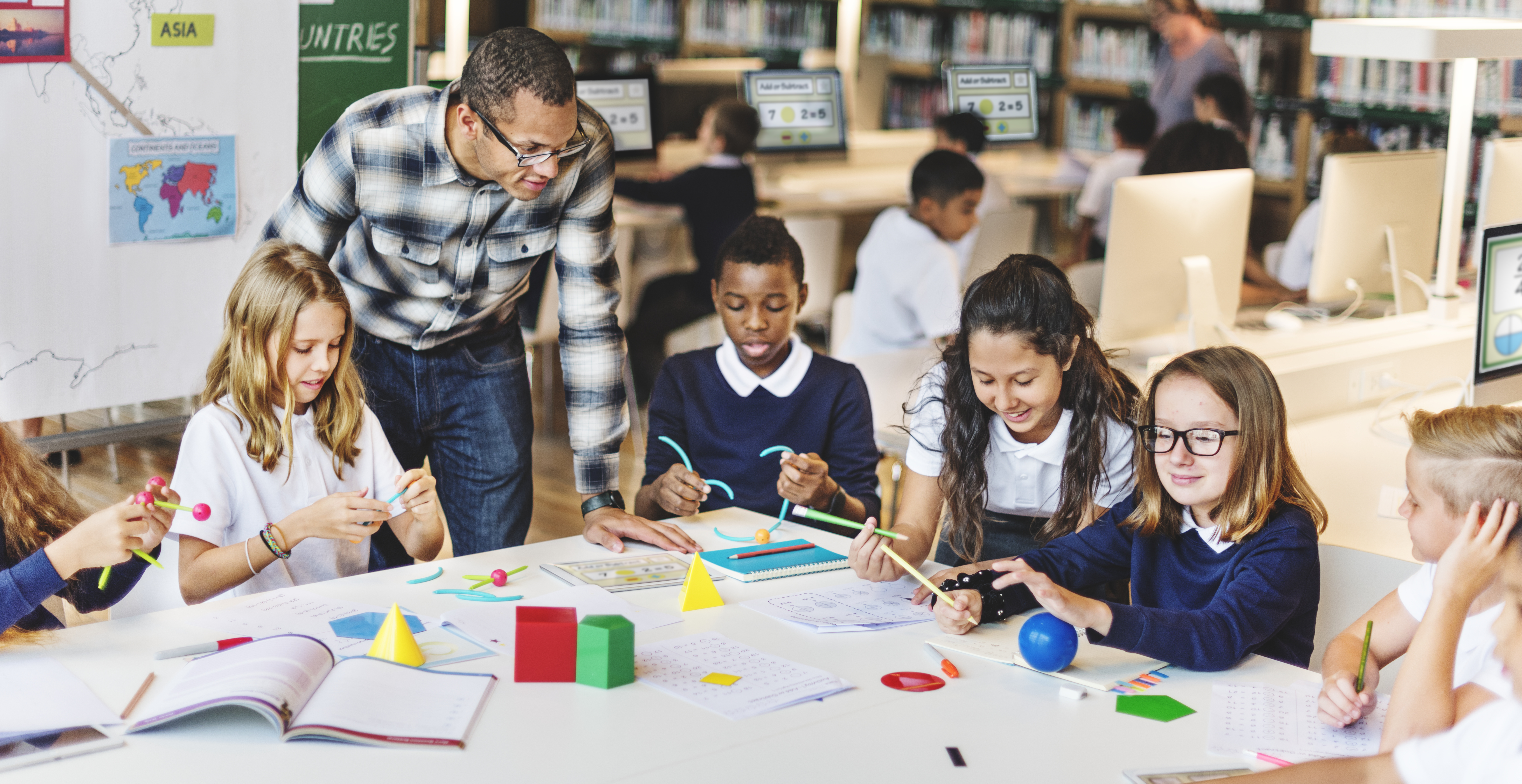 Elementary students at a table working with math manipulatives with a teacher assisting