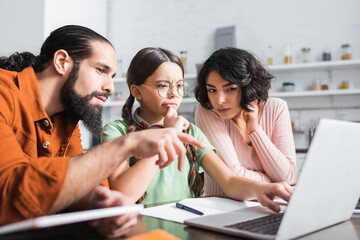 Pensive girl using laptop near hispanic parents during online education at home