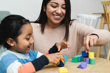 Latin American mother and son child having fun playing games with wood toy bricks at home - Family time together