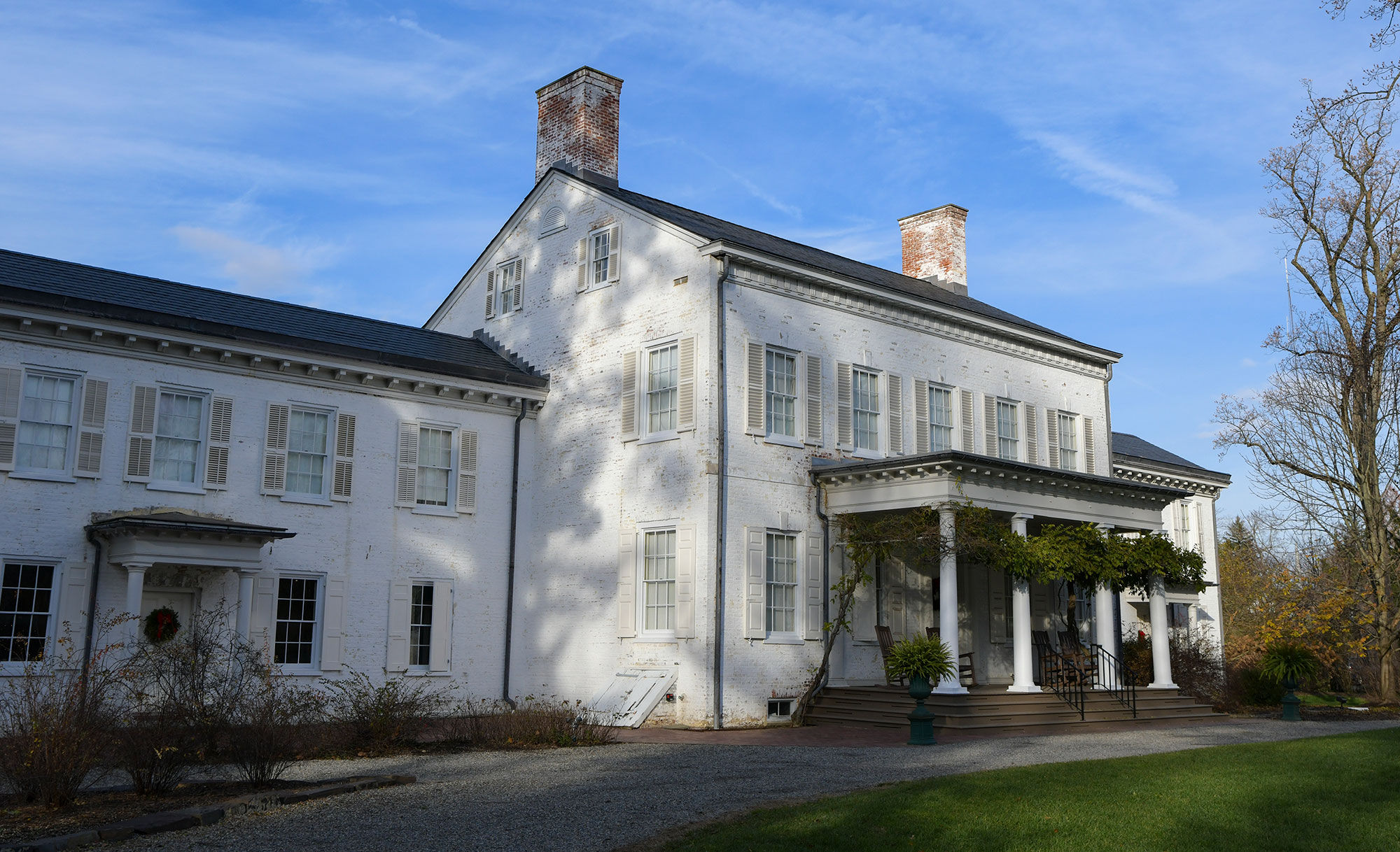 Bright blue sky and exterior photo of Morven, New Jerseys first Governors residence. White painted brick mansion with front portico, greenery wraps four columns.