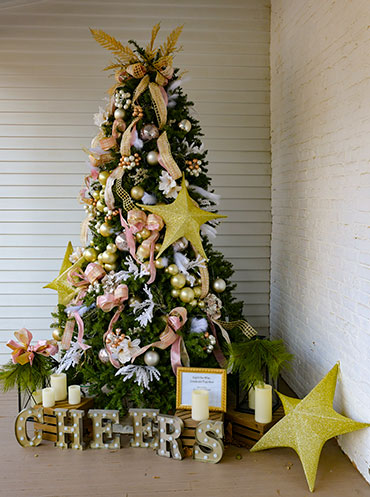 photo - Stony Brook Garden Clubs “Light the Way” Christmas tree on Morvens Back Porch features gold and cream balls and pink ribbons and bows. Displayed are gold stars, electric candles and large letters at the base of the tree spelling out the word "cheer