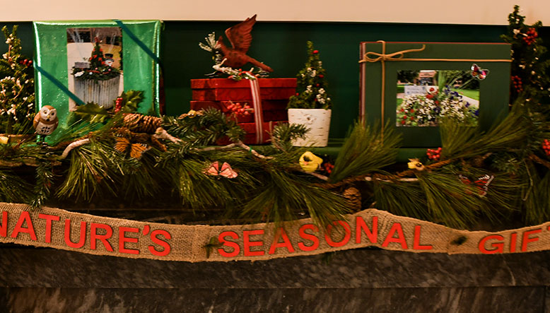 photo - A close photo of a decorated mantelpiece entitled “Natures Seasonal Gifts” by Nottingham Garden Club of Hamilton Township. Realistic bird figures and brightly colored packages with evergreens and berries are creatively displayed.