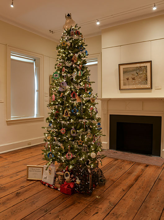 photo - “A Merry Cocker Spaniel Christmas” tree by the American Spaniel Club/Southern NJ features hand made ornaments of Cocker Spaniels among bright lights. The room is beige with a wildlife painting above a fireplace.