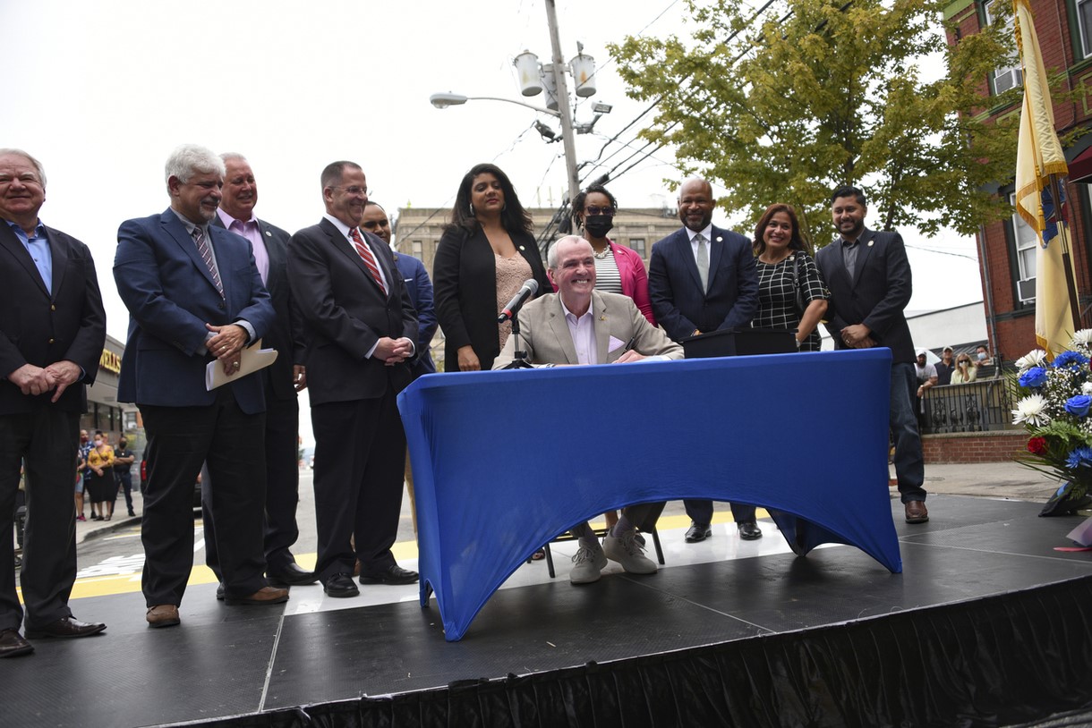 photo: Governor Phil Murphy sitting, behind a table signing legislation 