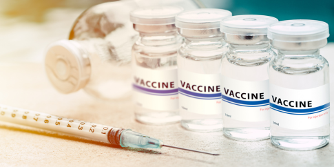 A syringe laying next to four vials of vaccines