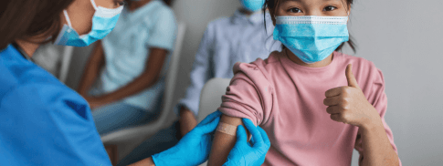 A child giving thumbs up after receiving a shot from a health care provider.