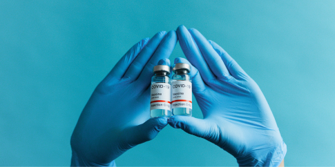 Hands forming in the shape of a diamond holding two vials of COVID-19 vaccine