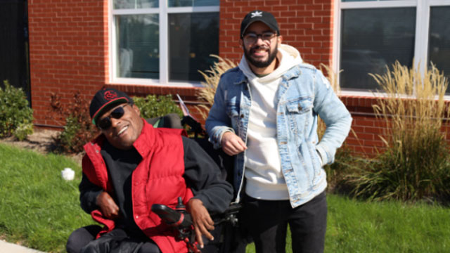 Man standing next to a person in a wheelchair.