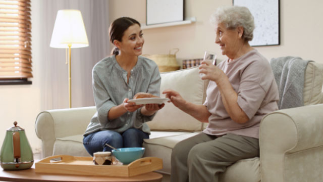 Two women sitting on the couch and the elder one is being taking care of.