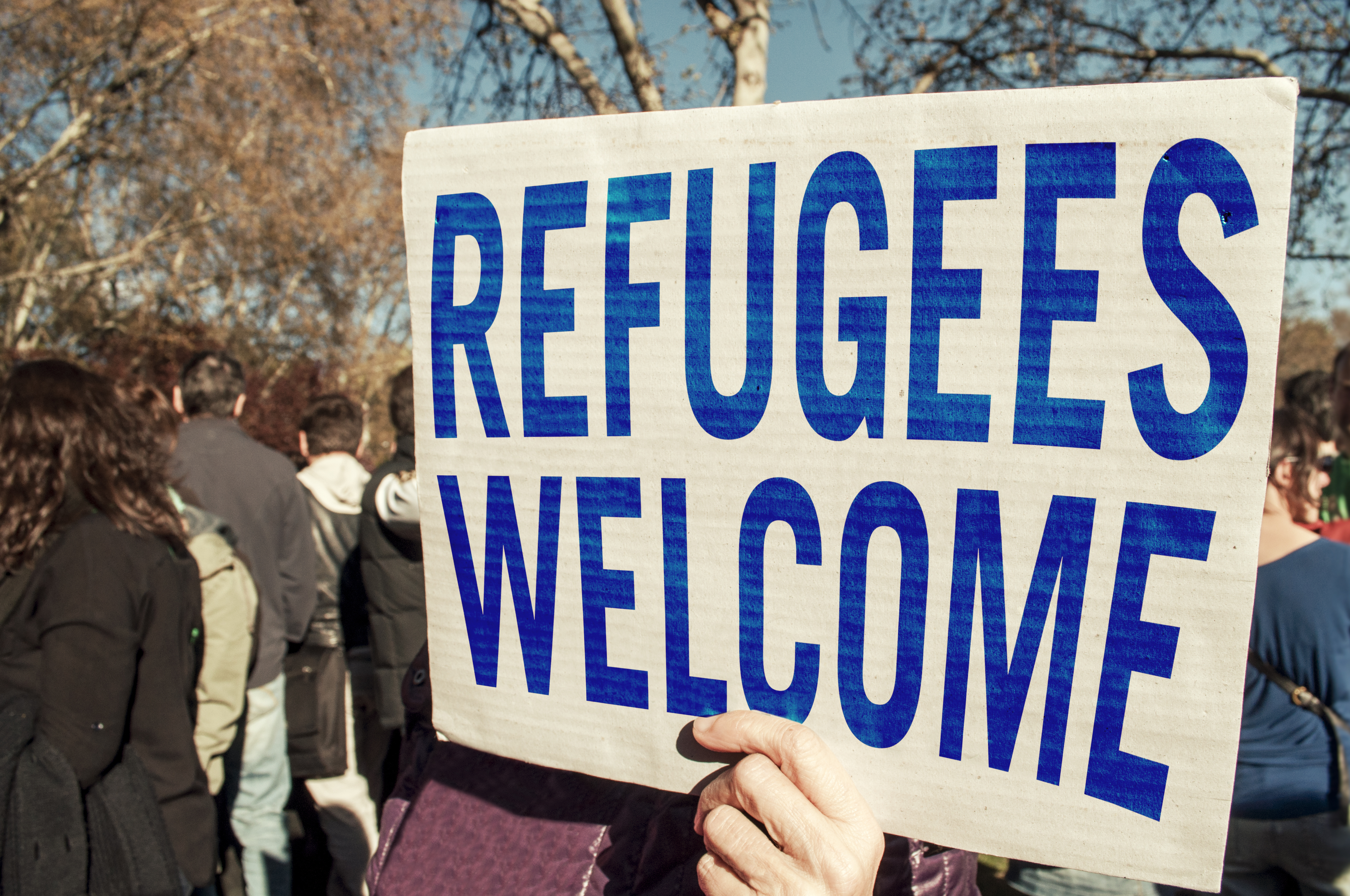 Refugees Welcome banner is held by a protestor