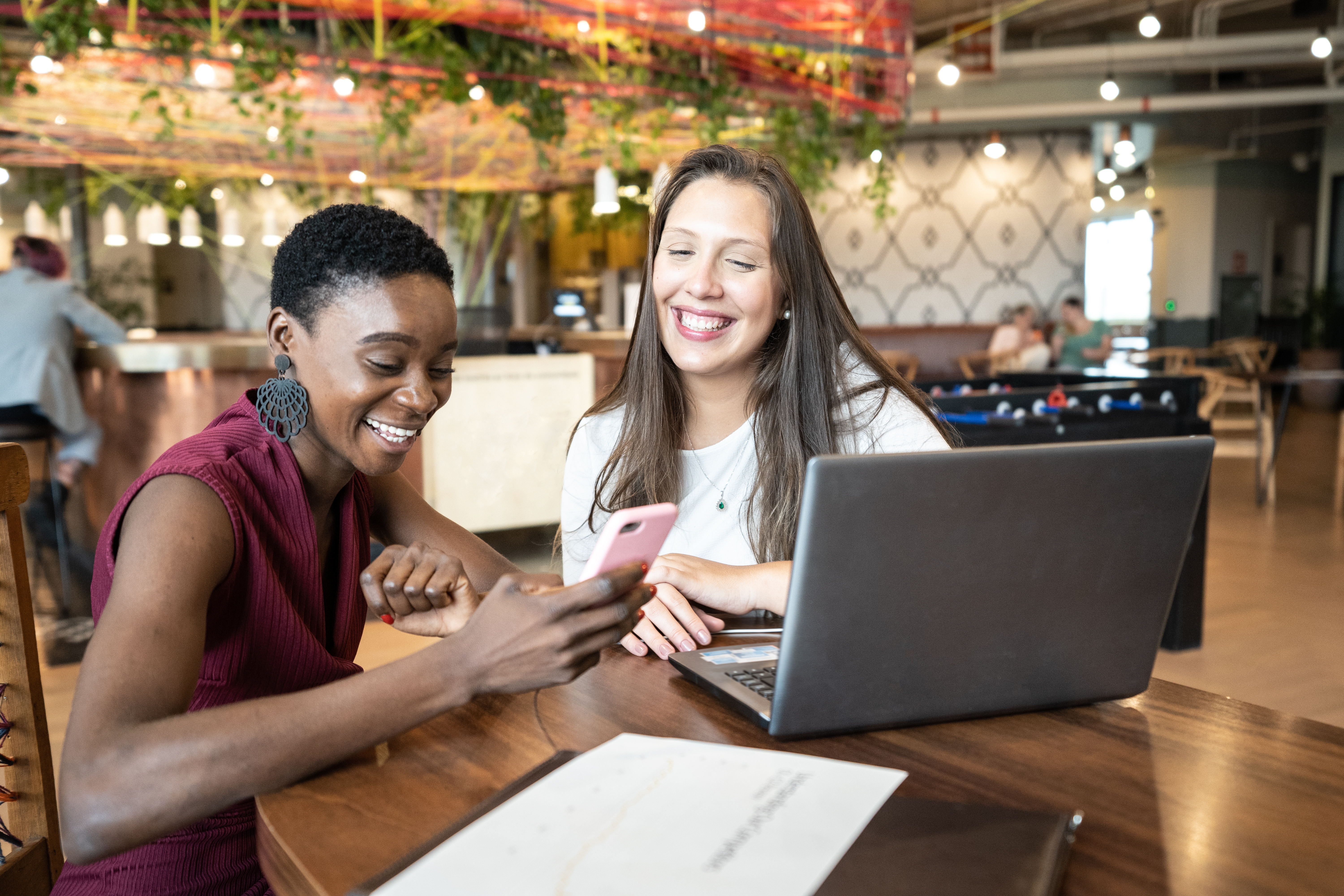  Two women are sitting by the table with laptop and smartphone in the cafe