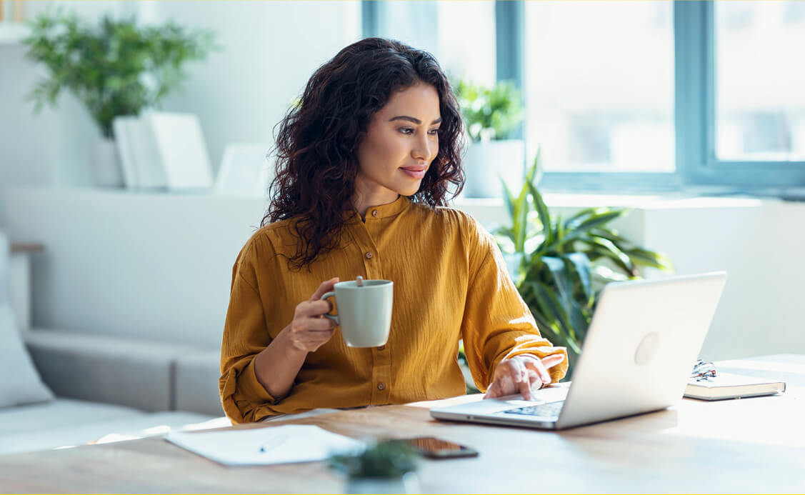 A woman holding a cup while working on the laptop