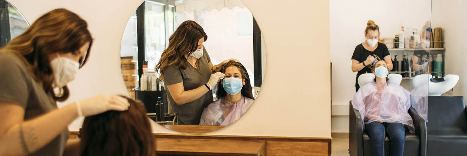 woman in a beauty salon servicing clients, all wearing face masks