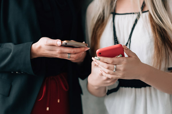 two women in business attire standing near each other, looking at each other's cell phones