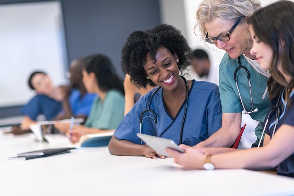 nursing student smiling while sitting at table with another student and professor