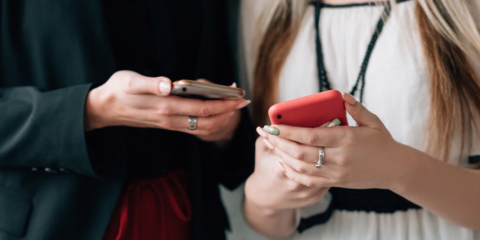 two women in business attire standing near each other, looking at each other's cell phones