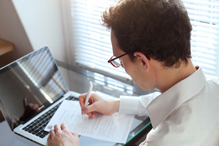 man at a desk looking at a form and computer