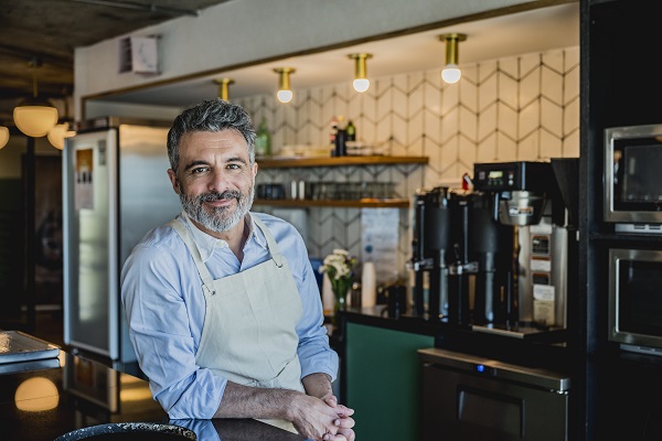 Man wearing apron and leaning on counter in coffee bar