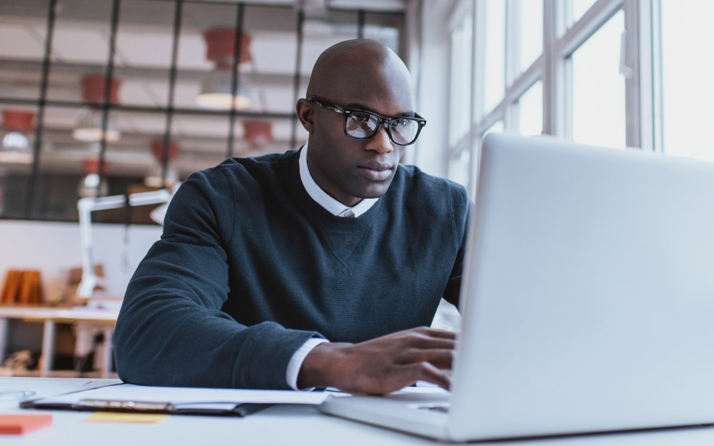 An African-American man sitting at a computer at a desk in a bright, modern office