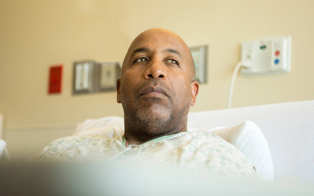 African-American male patient lying in a hospital bed, looking contemplative
