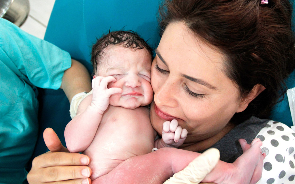 A smiling woman who just gave birth in a hospital holding her baby for the first time