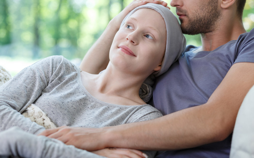 Woman undergoing chemotherapy for cancer being embraced by her male partner on a sofa