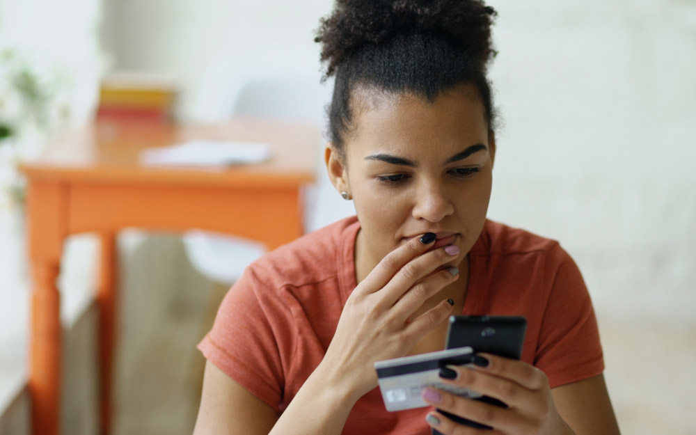 An African-American woman holding a debit card, looking thoughtful