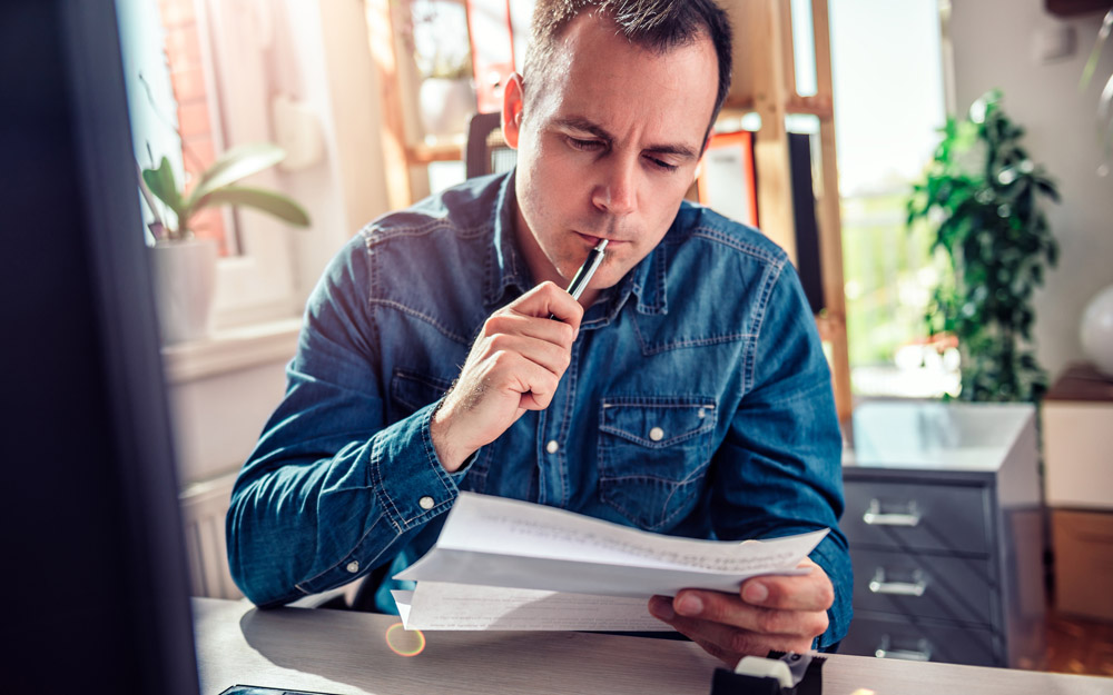 A man sitting at a desk, looking at mail he opened, seeming a bit confused