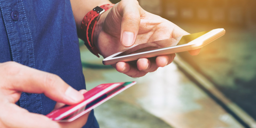 A close-up of a man's hands holding a debit card and a smartphone