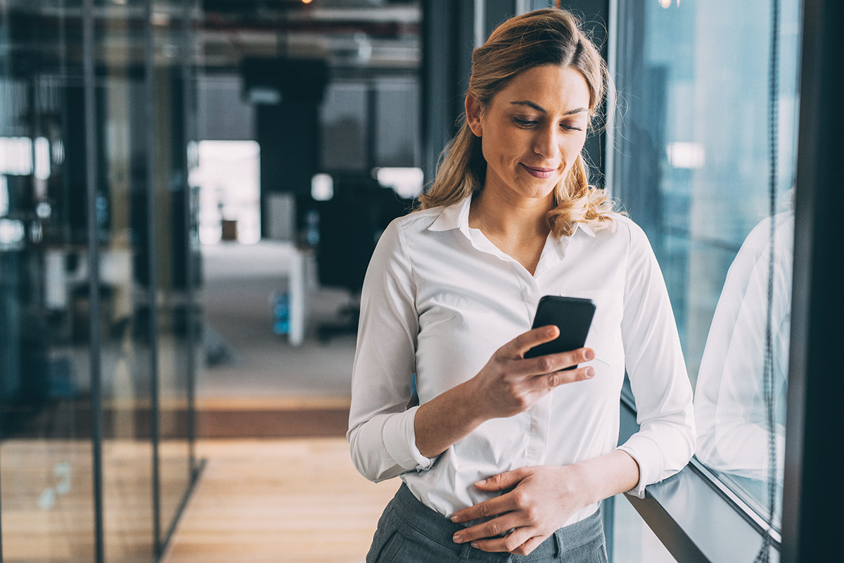 a woman in an office setting looking at her phone with her hand casually on her lower abdomen