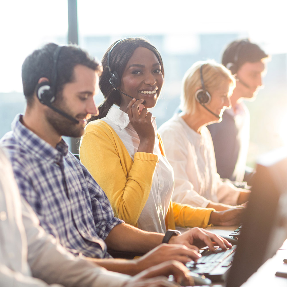 A picture of a row of workers sitting at computers wearing phone headsets, with an African-American woman in the center facing the camera and smiling