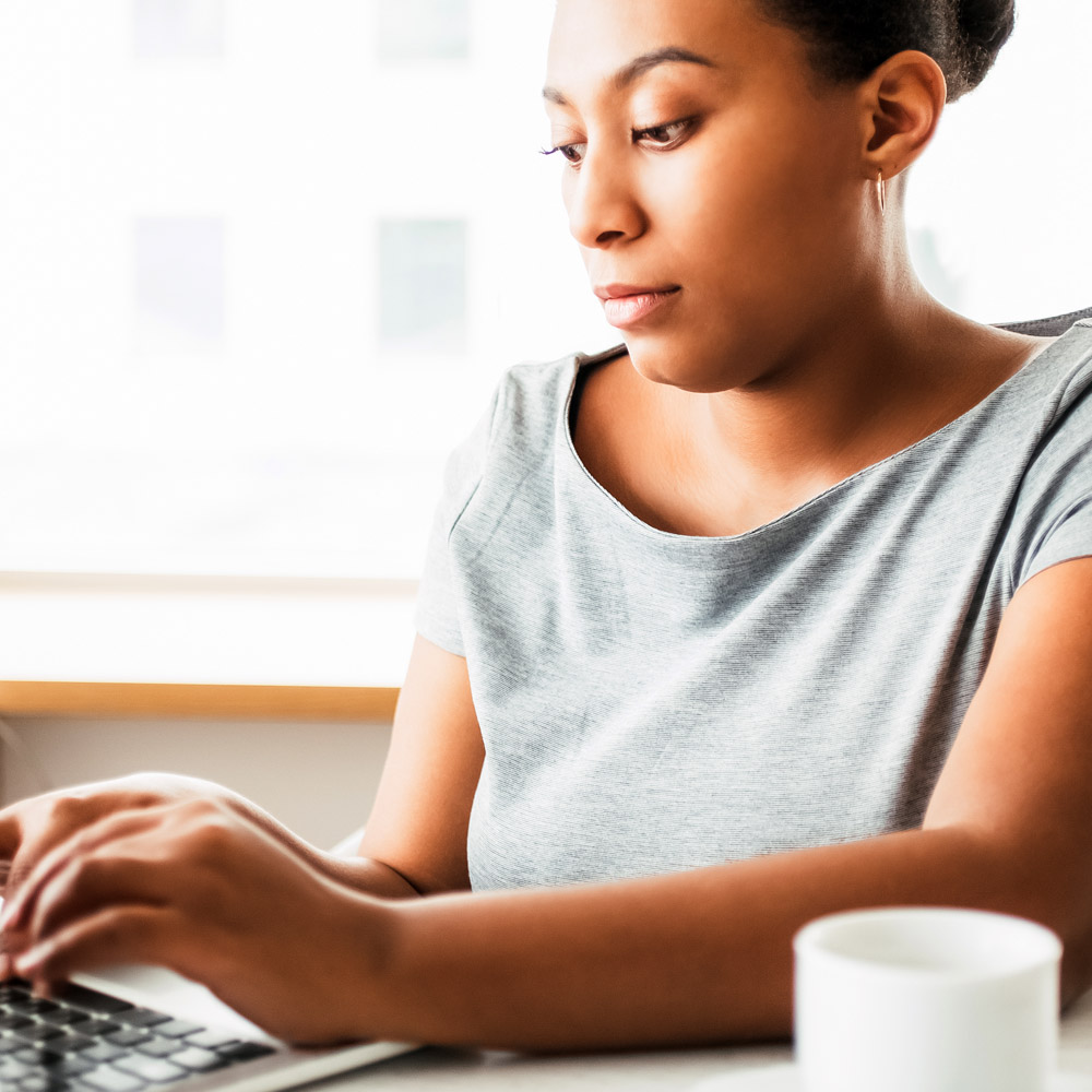 An African-American woman sitting at a desk with a computer, typing