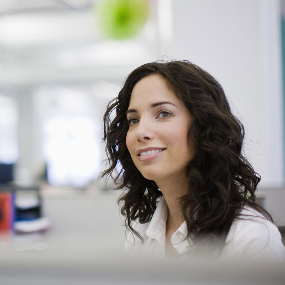 picture of a female office worker sitting at her desk, smiling