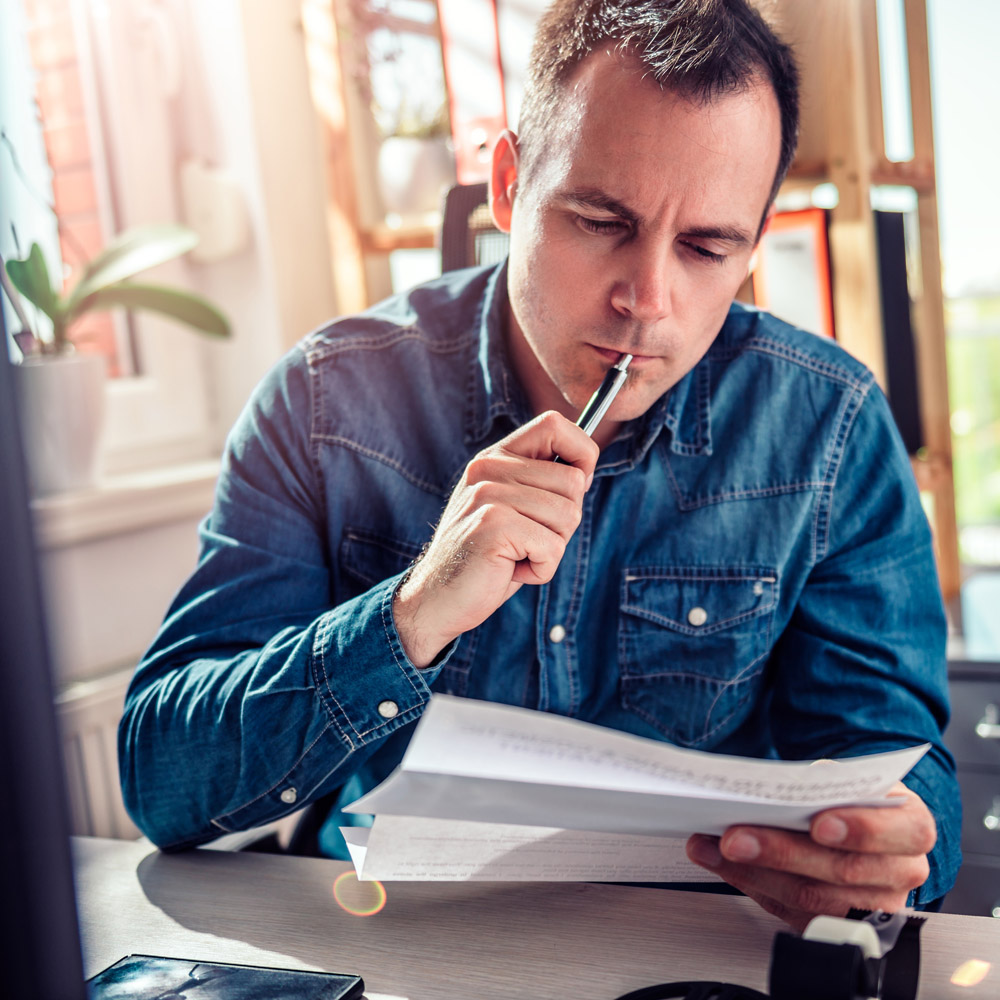 A man sitting at his desk opening a letter, looking confused