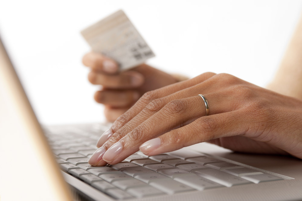 A woman holding a debit card while typing on a computer keyboard