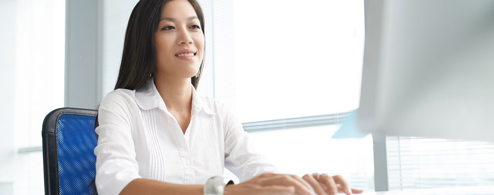 Smiling Asian woman sitting at a desk in front of a computer in a modern office