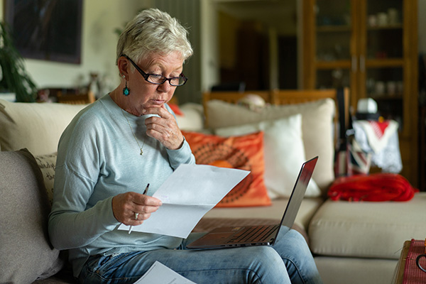 a elderly woman looking puzzled reading a letter in front of her laptop computer