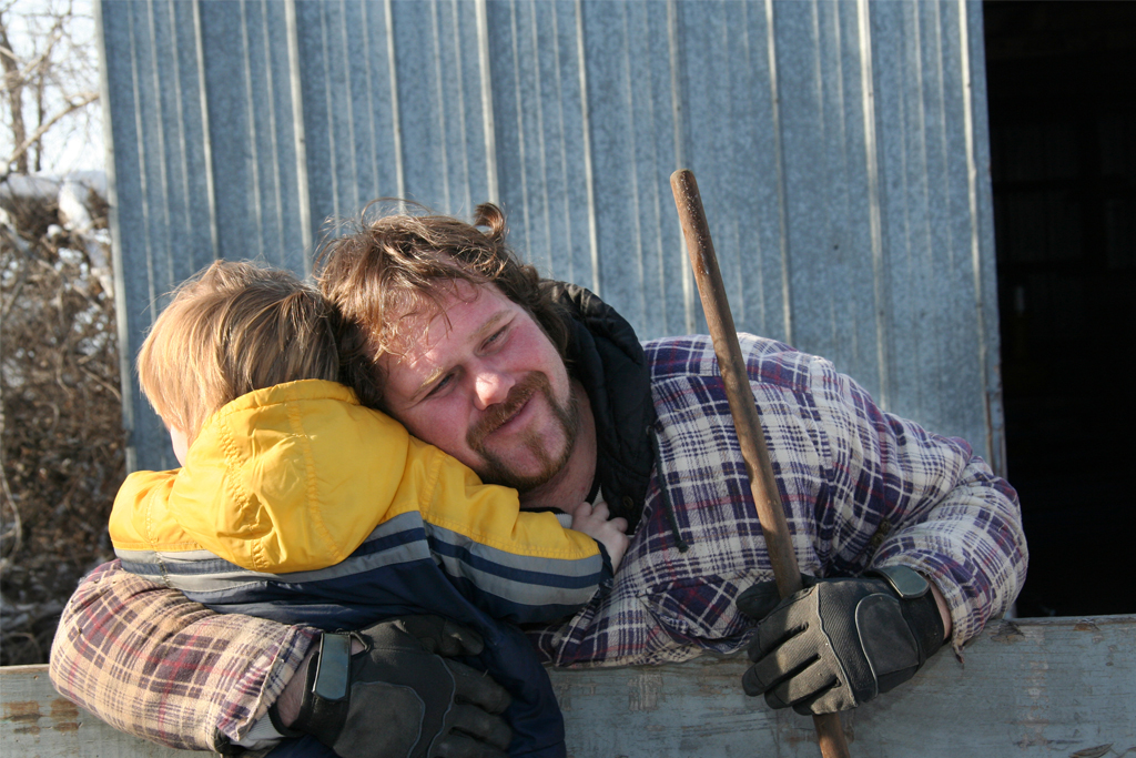 man taking a break from yard work to hug his young son