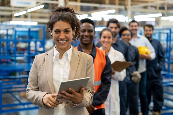 Female manager at a factory holding a tablet with team of blue collar workers, engineers and inspectors