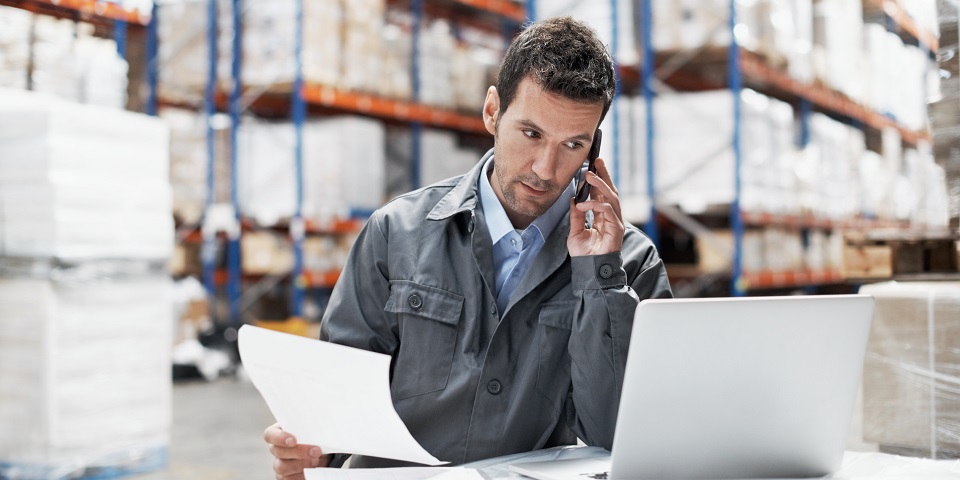 Man on phone at computer in warehouse