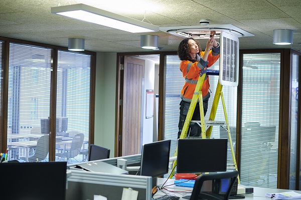 Woman fixing light fixture in office