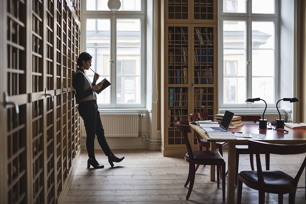 Woman leaning against bookshelf in library