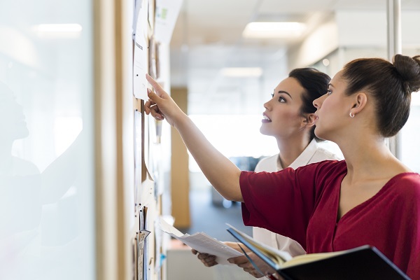 Two woman looking at flyers on office wall